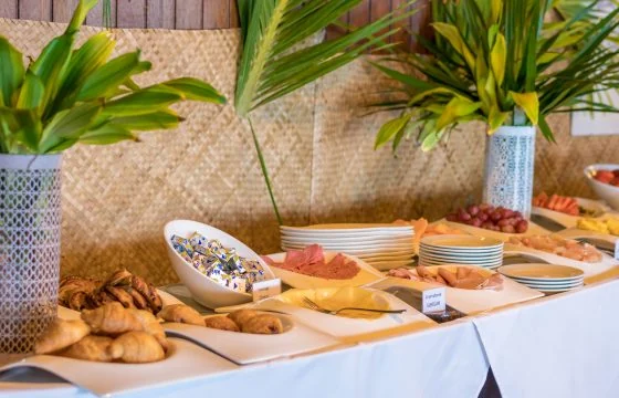 Un buffet avec viennoiseries, fruits, assiettes et feuillages au restaurant du Mahana.