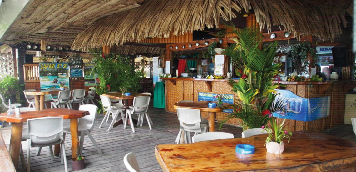 Tables en bois, chaises blanches et comptoir sous la toiture végétale du Huahine Yacht Club, à Fare.